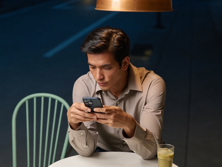 A man at a cafe table in Kuala Lumpur, phone held low in both hands