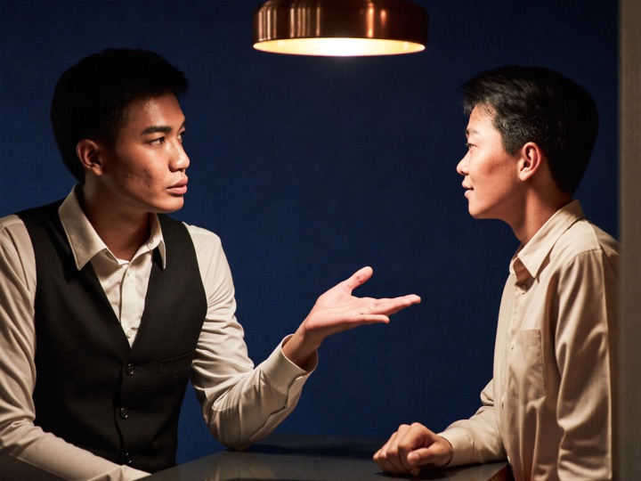 A host in a waistcoat talking across a counter with a guest on a weekend evening