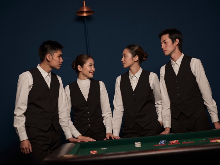 Four dealers in black waistcoats standing together at the corner of a gaming table before opening