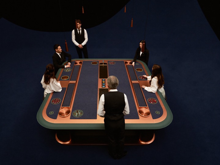 A gaming pit seen from above, four tables in a row with dealers standing at each