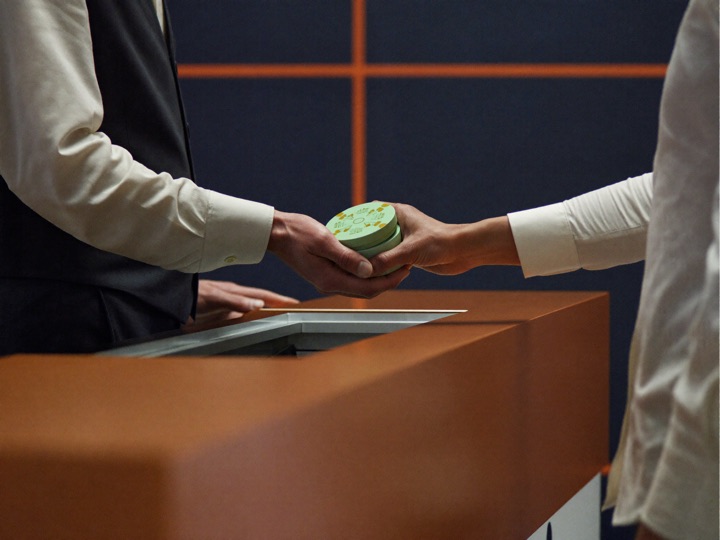 A teller in a waistcoat sliding copper and mint chips across an open cashier counter into a guest's hand