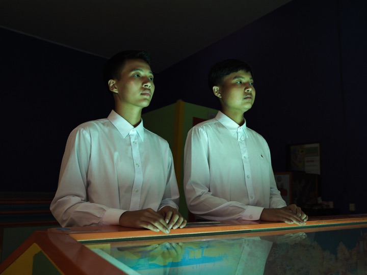 Two young adults in shirts at a wide arcade fish cabinet, blue water light across their faces