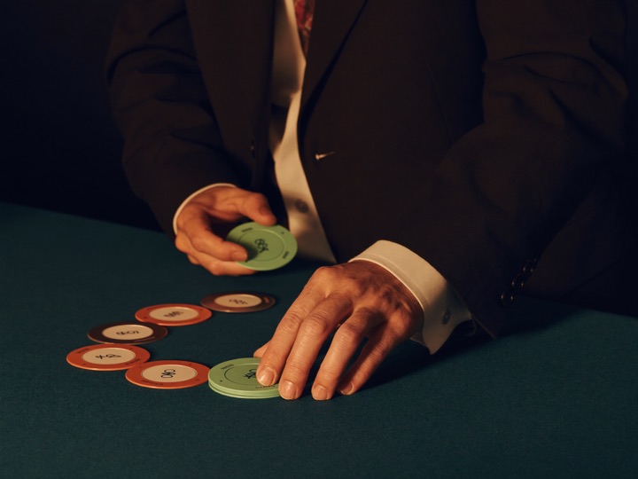A host in a dinner jacket sliding a small stack of chips across dark felt